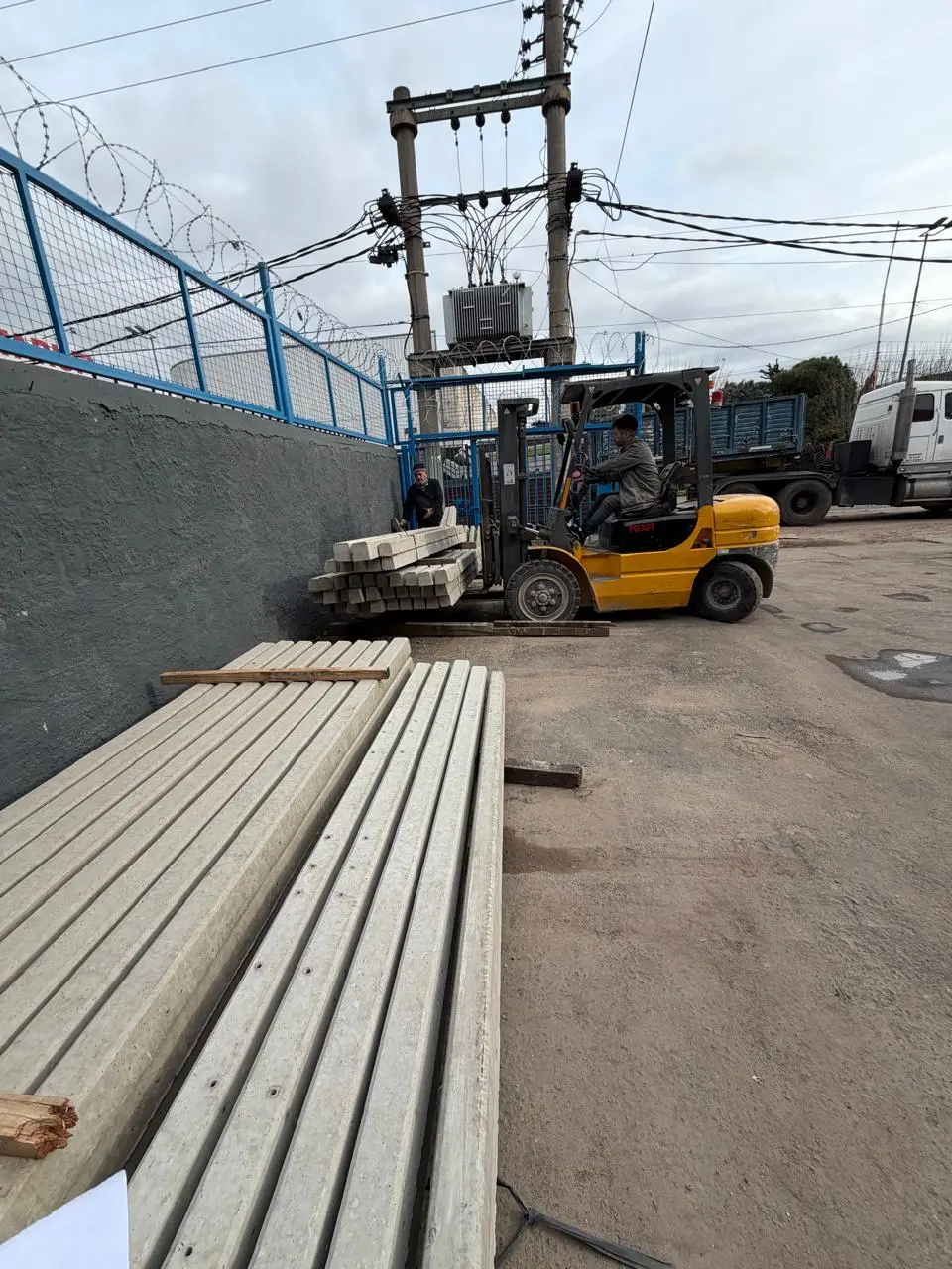 Un autoelevador cargando un atado de postes de hormigón en el patio del depósito de Casa Ledesma, con más postes apilados en el piso