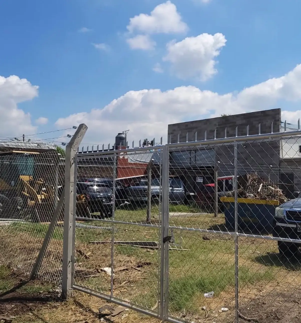 Portón de dos hojas de caño con pinches de seguridad arriba, ya colocado en el frente de un terreno, con el poste esquinero de hormigón a la izquierda
