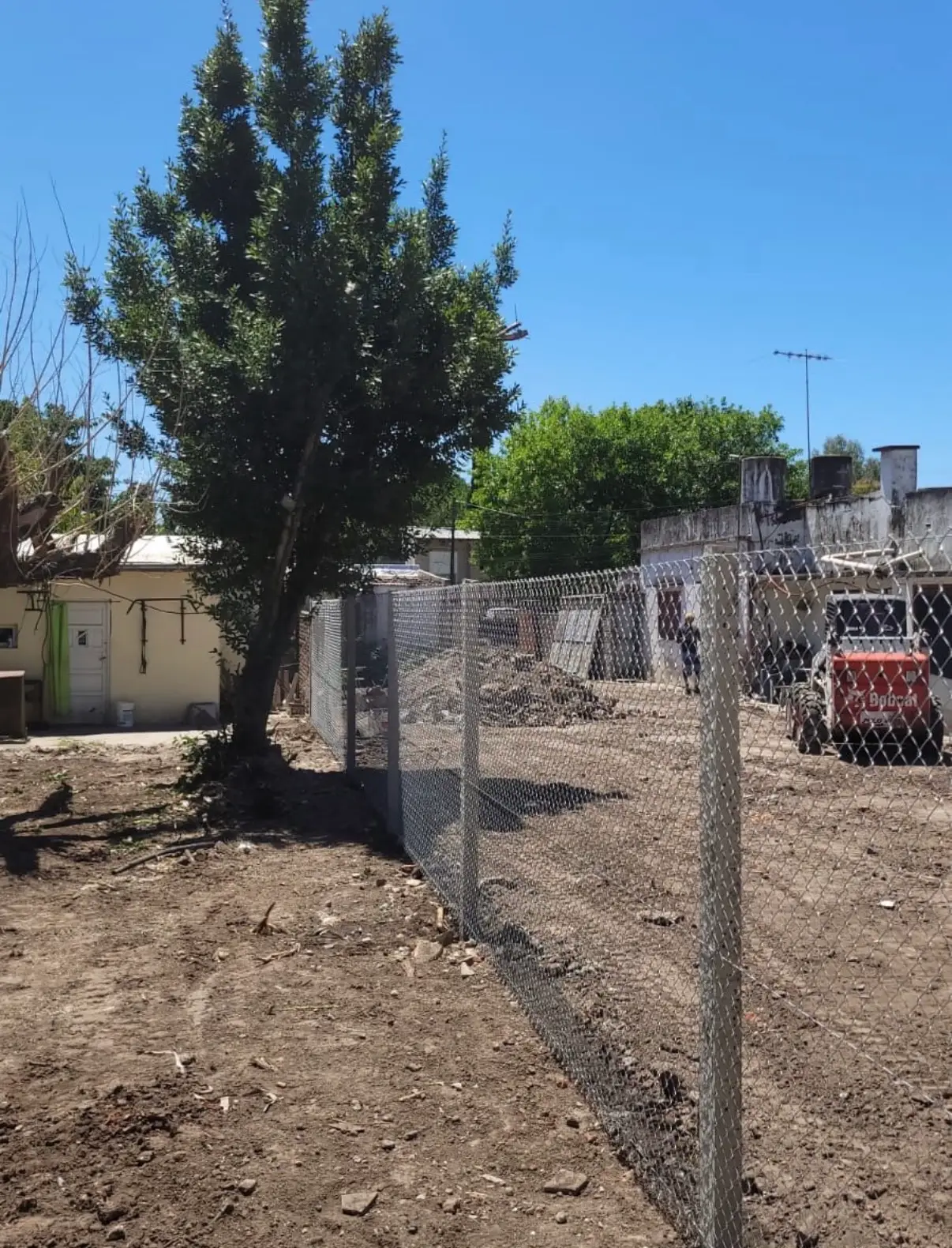 Alambrado de tejido romboidal sobre postes rectos de hormigón, recién instalado dividiendo un terreno, con una obra al fondo