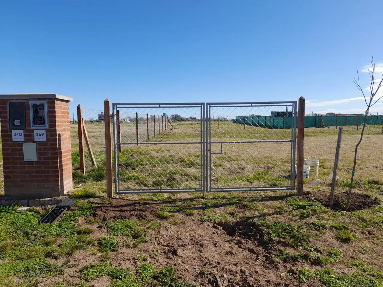 Portón de dos hojas de caño colocado en la entrada de un lote, con el alambrado de tejido siguiendo la línea a los costados