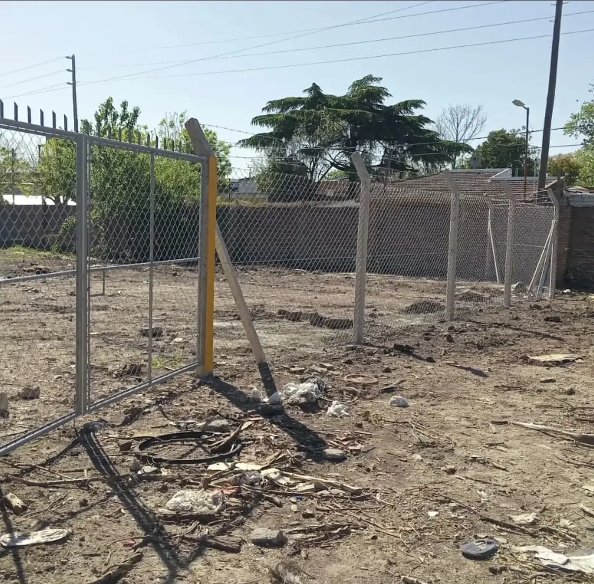 Alambrado olímpico a medio instalar: los postes de hormigón curvados ya plantados en línea, uno apuntalado con una madera, y el tejido todavía sin colgar