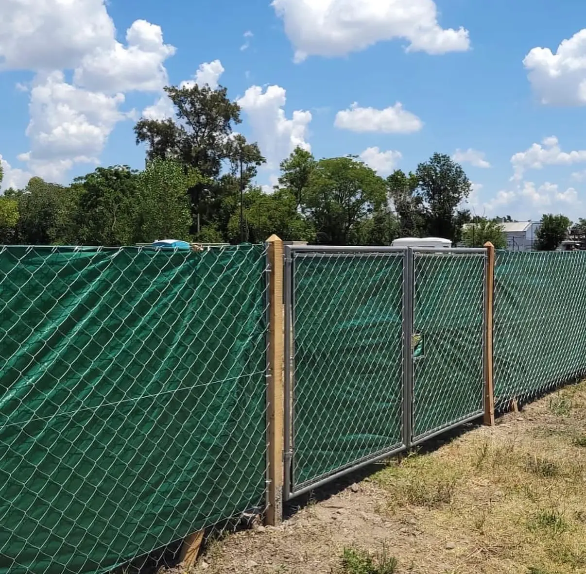 Alambrado de tejido romboidal sobre postes de quebracho con media sombra verde puesta por detrás, y un portón de dos hojas de caño en el medio del recorrido