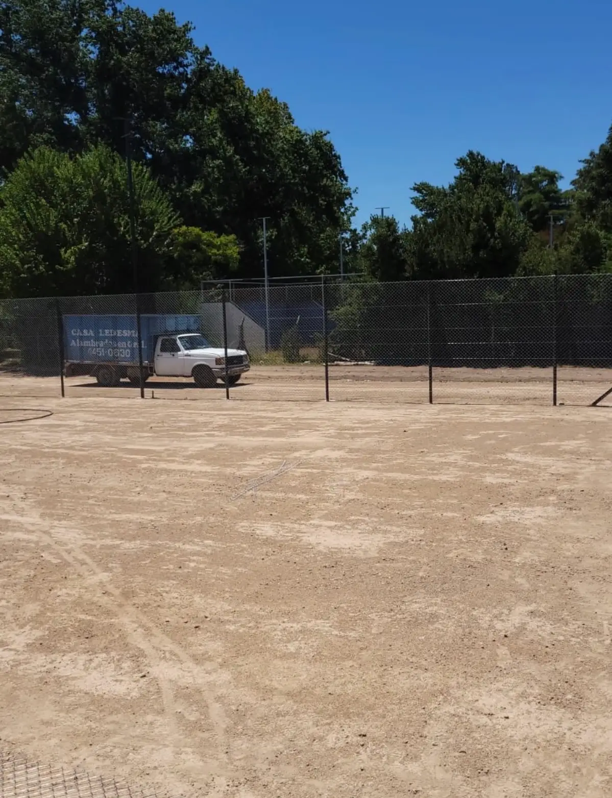 Alambrado perimetral alto de una cancha, con el camión de Casa Ledesma estacionado del otro lado