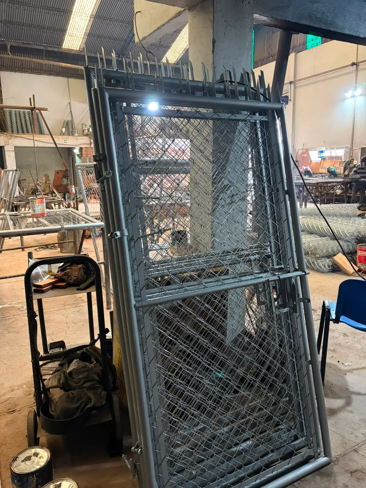Portón de caño con tejido pintado de gris oscuro, con pinches de seguridad, en el taller
