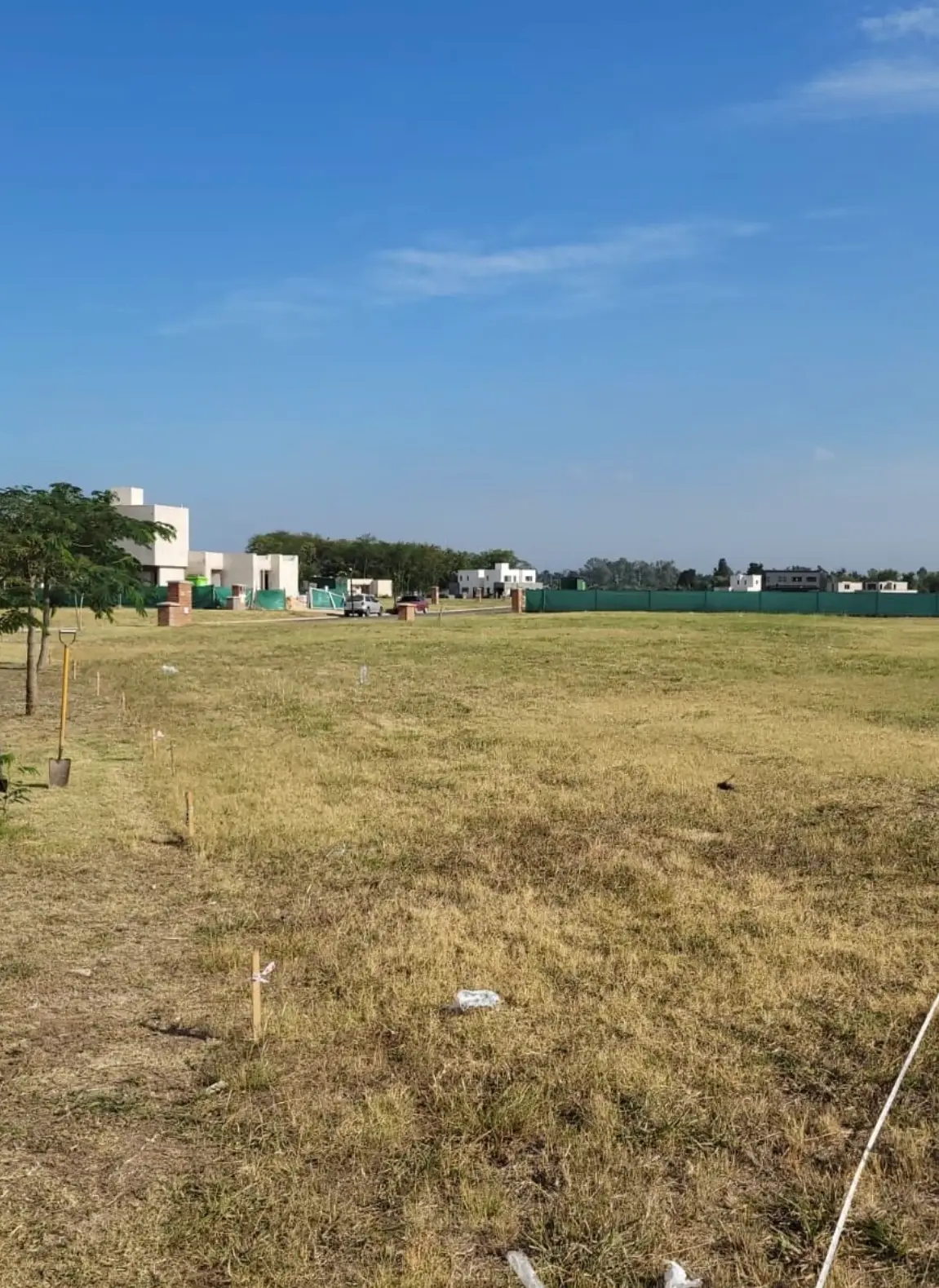 Terreno con la línea del alambrado ya replanteada: estacas de madera clavadas en fila y un hilo tendido marcando el recorrido, con una pala apoyada